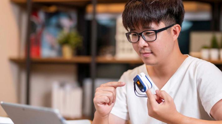 Person in front of laptop with remote medical device on finger Person in front of laptop with remote medical device on finger